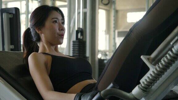 年轻有魅力的亚洲女人在健身房训练腿运动女子训练她的四头肌在机器压在健身房慢动作保健、健身和健美