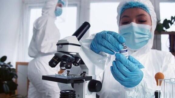 快乐的女性临床实验室科学家在防护服和盾牌与新疫苗烧瓶战胜疾病的希望