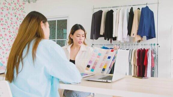 两位亚洲女性时装设计师或服装师集思广益用平板上的面料和草图来讨论新系列的设计一起在工作室工作