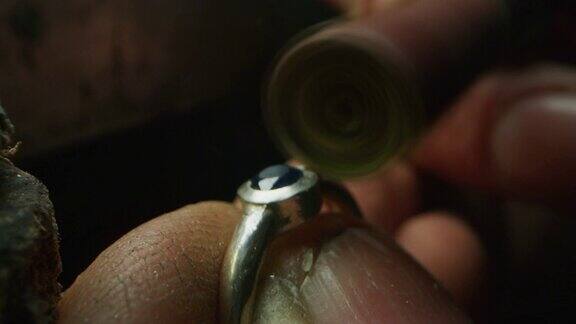 慢镜头近距离的经验丰富的金匠抛光一个手工珠宝戒指与珍贵的宝石在一个车间