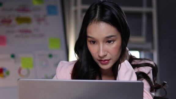 在办公室工作的忙碌的亚洲女性在办公桌前用笔记本电脑工作时伸展身体放松