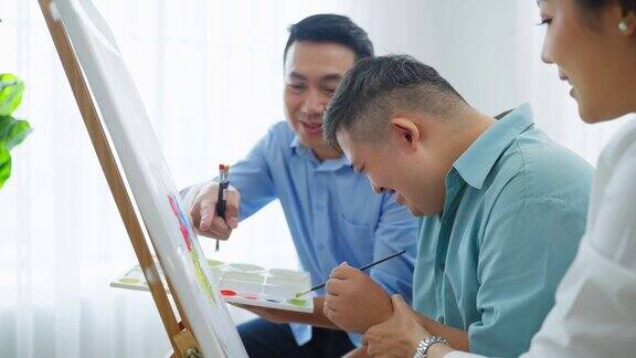亚洲幸福家庭与唐氏综合症儿子在客厅画画美丽慈爱的父母照顾和教患有自闭症或特殊需要的年轻人在家室内绘画艺术品
