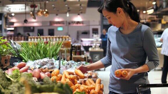 漂亮的女人在超市买胡萝卜蔬菜和水果