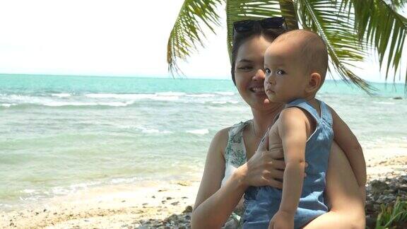 亚洲母亲走在沙滩上抱着婴儿的男孩