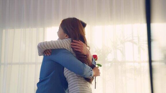亚洲青年惊喜送玫瑰给美丽的女友迷人浪漫的新婚男女花时间在家里一起庆祝周年纪念日和情人节