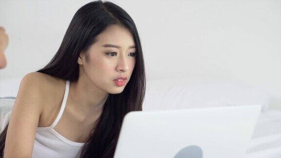 美丽的亚洲年轻女子躺在床上使用笔记本电脑在卧室休闲和放松自由职业者与女孩工作笔记本沟通慢动作