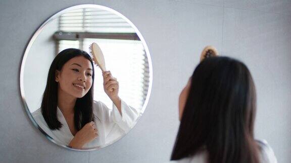 快乐的韩国女人在浴室里看着镜子梳头发