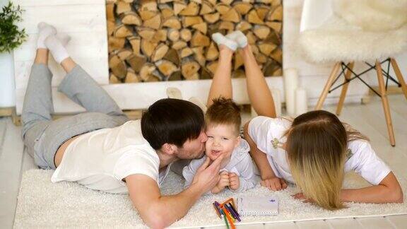 一个年轻的家庭带着小儿子在地板上玩耍在客厅里亲吻微笑着的他