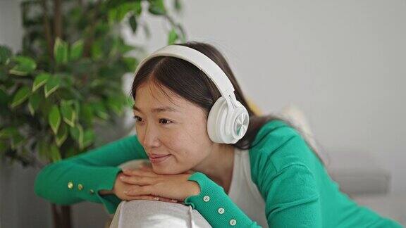 年轻的中国女子在家里的沙发上放松地听音乐