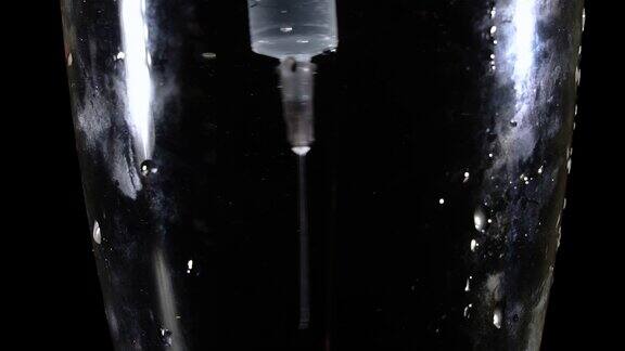一只医用注射器漂浮在一杯深水中它在水中旋转特写镜头