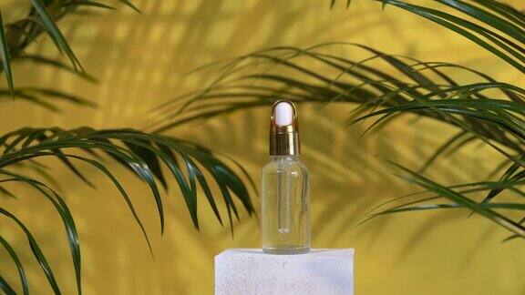 玻璃瓶中的血清停留在白色的讲台上黄色的背景与棕榈叶和阴影香薰油天然化妆品
