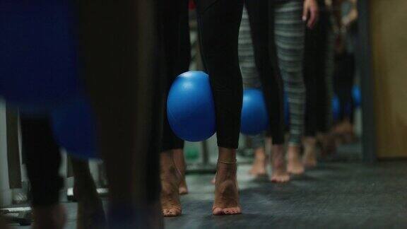 一群多民族的妇女在健身室的课堂上用健身球在她们的小腿之间跳动