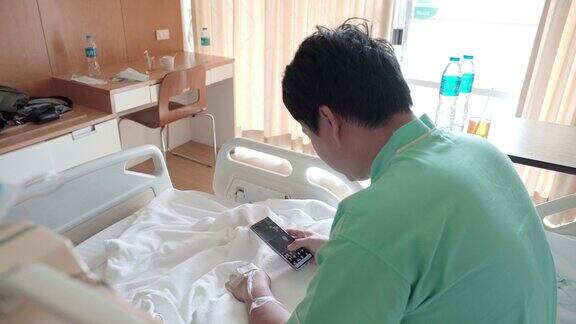男亚裔病人坐在病床上在病房里使用电话