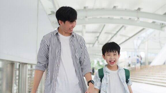年轻的亚洲男孩拿着五颜六色的购物袋和父亲一起走在购物中心购物的乐趣年终礼物的快乐年中促销和假日概念