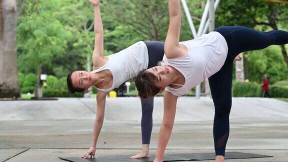 两个年轻的健身亚洲妇女练习瑜伽一起放松在城市公园