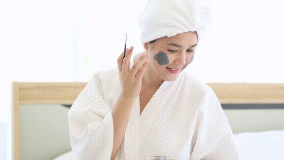 快乐美丽的女人在白色浴衣敷面膜皮肤护理和治疗