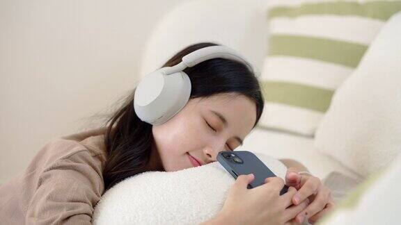 亚洲年轻女性躺在家里客厅的沙发上听音乐享受音乐播放列表