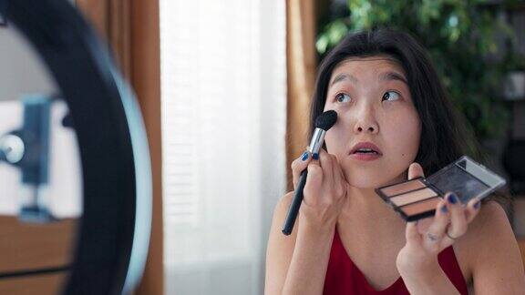 作为一名年轻的亚洲美女、视频博主、在线内容创造者和化妆师她使用古铜色化妆品和荧光粉勾勒面部轮廓突出脸颊