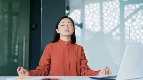 一名亚洲女性坐在办公室里闭着眼睛冥想