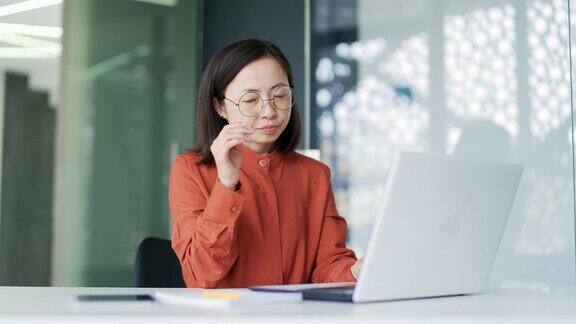 劳累过度的亚洲女商人在现代办公室里坐在工作场所用笔记本电脑工作时眼睛疲劳