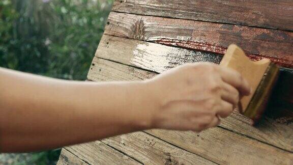 户外在她的花园妇女用画笔在木板上涂木材保护油的手妇女用画笔在深棕色的木板上手绘
