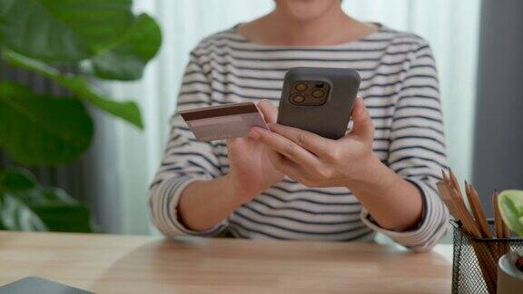 近距离拍摄女性的手拿信用卡和使用智能手机在家庭办公室网上购物