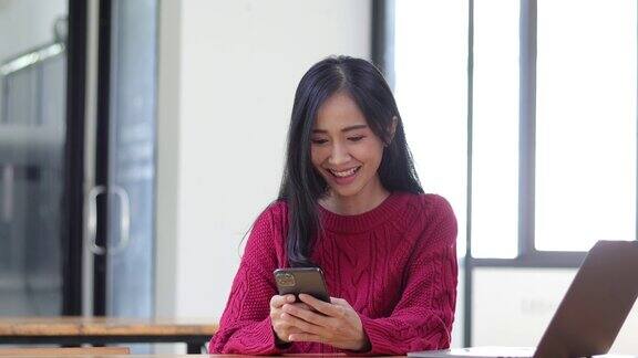 快乐的亚洲女性在家庭办公室使用智能手机女孩使用智能手机通过手机与朋友聊天