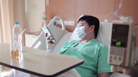 男亚裔病人在医院病床上用手机发短信