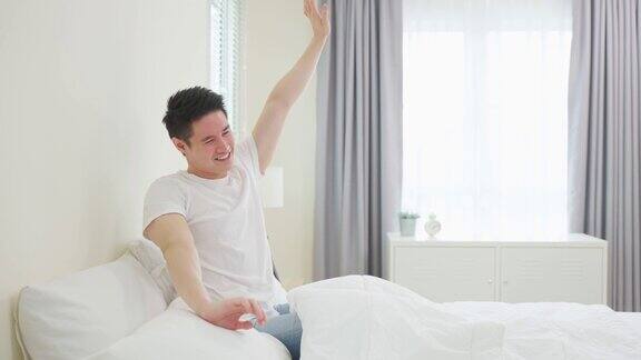 穿着睡衣的亚洲帅哥早上快乐地醒来迷人的年轻人微笑感觉快乐和放松然后伸展身体后从床上的卧室在家里