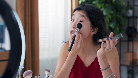 作为一名年轻的亚洲美女、视频博主、在线内容创造者和化妆师她使用古铜色化妆品和荧光粉勾勒面部轮廓突出脸颊