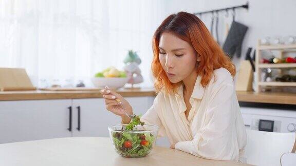 亚洲有吸引力的女人在家里厨房的桌子上吃绿色沙拉年轻美丽的素食女孩感到快乐享受早餐蔬菜健康的食物在家里减肥健康