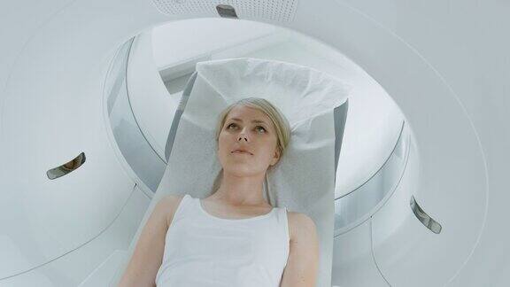 一个女性病人的特写肖像躺在一个CT或MRI扫描床是移动机器扫描她的身体和大脑在医疗实验室的高科技设备提升相机拍摄