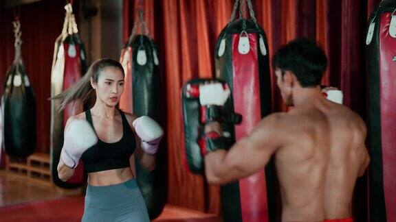 一名身着运动服的亚洲年轻成年女子在健身房与她的拳击教练练习拳击