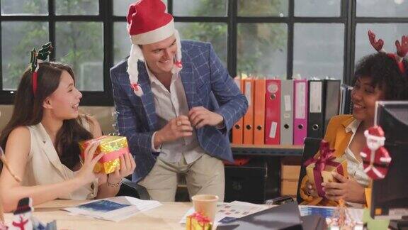 年轻的商务团队在办公室里庆祝节日都戴着圣诞老人的帽子给同事送礼物办公室里相爱的漂亮年轻人交换礼物盒庆祝