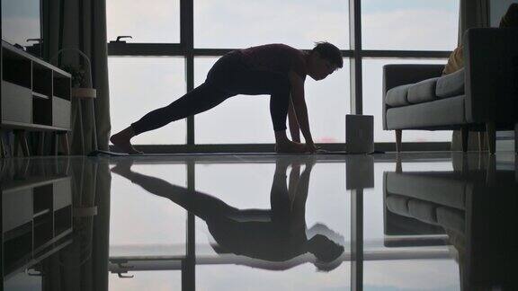 周末的早晨亚洲中国美女在靠近窗户的客厅里坐在瑜伽垫上在家锻炼