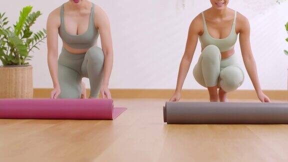 两个年轻运动员展开瑜伽垫准备在家庭工作室锻炼的特写女人滚下地板上的瑜伽垫瑜伽器材健康生活保持健康观念缓慢的运动