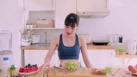 一个穿着运动服的亚洲女人在厨房里快乐地扔着蔬菜沙拉散发着幸福的光芒她崇尚健康的生活方式通过令人愉快和营养的烹饪来促进健康