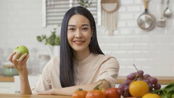 美丽的亚洲女人手里拿着橘子在厨房她看着镜头微笑着