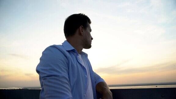 英俊的年轻人站在阳台上看日落思考着生活和问题