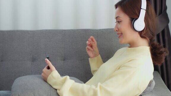 亚洲女性放松地坐在家里的沙发上拿着手机听音乐