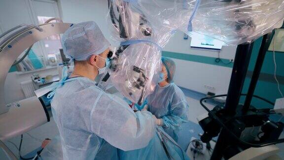 采用现代医疗设备的手术流程外科医生在显微镜下进行手术女助理在诊所里帮助医生