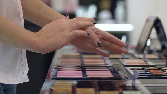 时尚的购物女孩选择新的胭脂粉底和测试在化妆品商店的手
