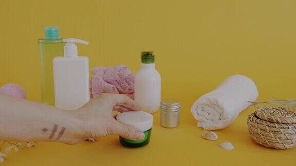 女性的手把身体护理霜放在黄色背景的有机化妆品和浴室配件的瓶子旁边