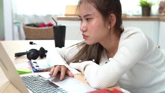 疲倦的亚洲年轻女商人困倦地使用笔记本电脑在家工作无聊的亚洲女学生趴在书桌上学习懒惰的家庭教育