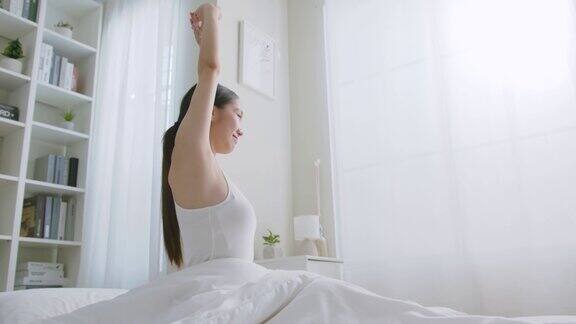 亚洲女性早上醒来坐在白色的床上伸伸懒腰感觉快乐又清新