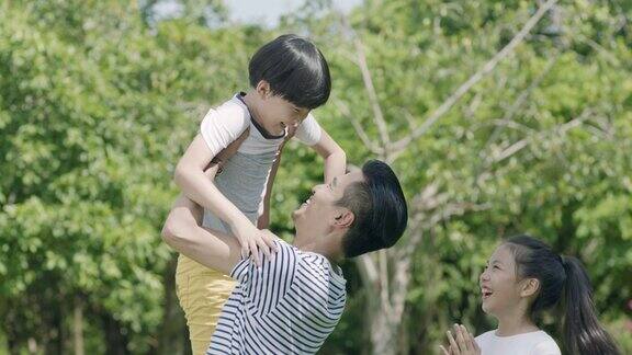 在慢镜头中一位亚裔父亲将儿子举在空中女儿在旁边