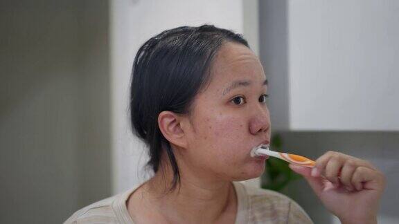 亚洲女人在浴室里刷牙镜子里映出她的牙齿