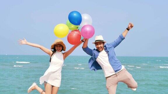 快乐的亚洲夫妇在海滩上拿着彩色气球生活方式概念慢镜头
