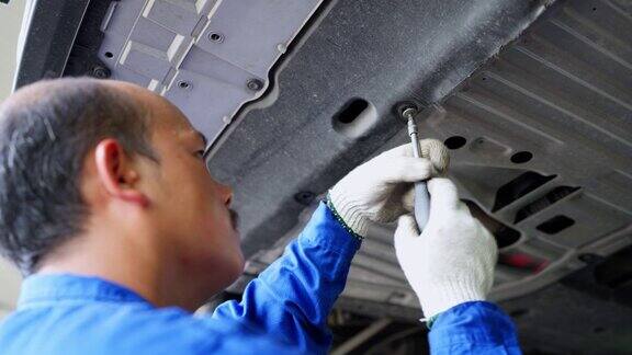 定期换油是对发动机的保养汽车维修机械师穿着制服戴着手套在修理厂用螺丝刀拆下发动机底盘换机油