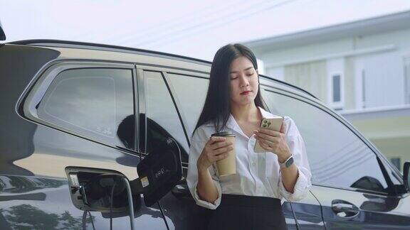 一名女子在家里等车充电时使用智能手机